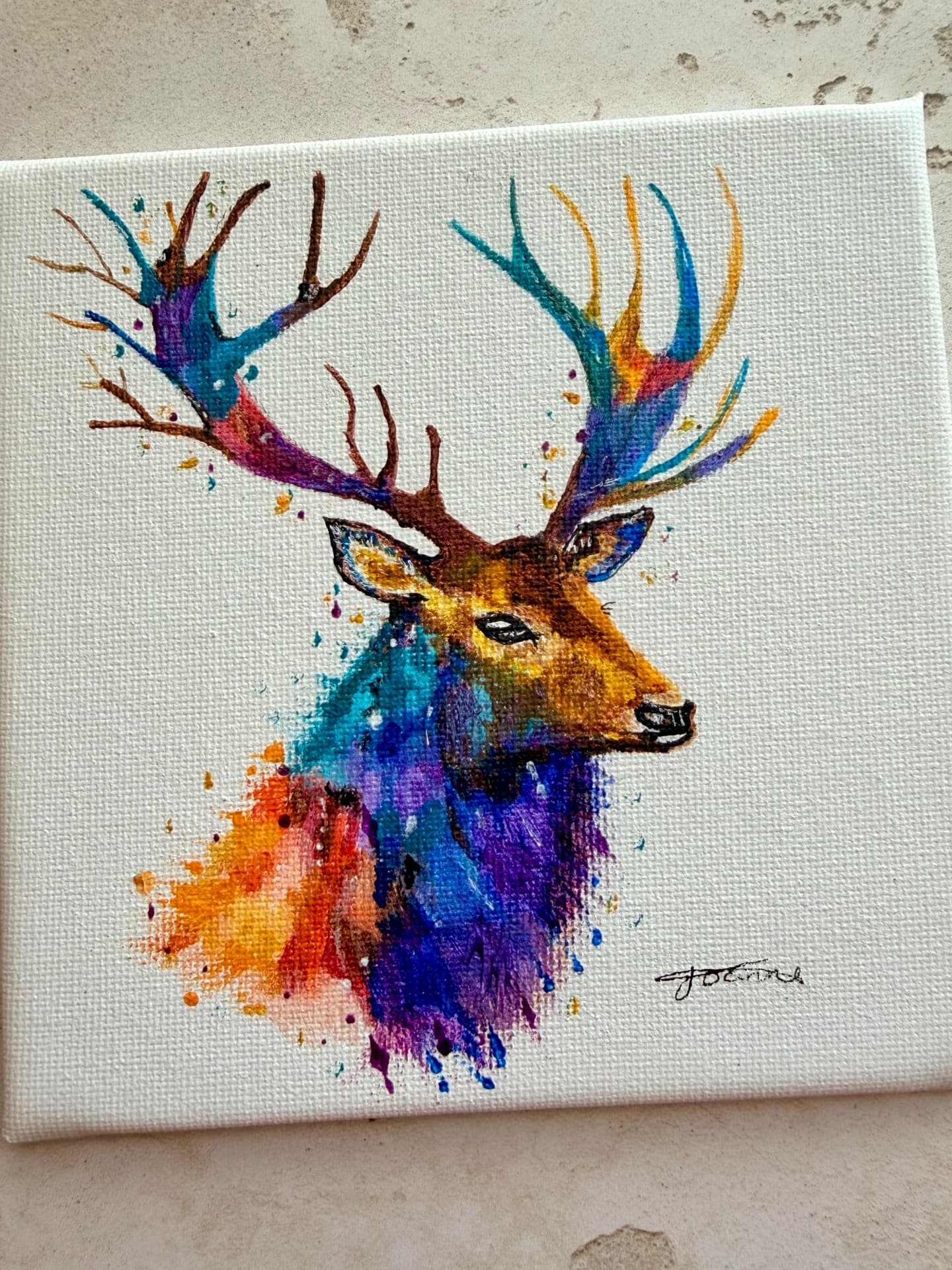 A hand-painted stag on canvas, its antlers and neck washed in bright teal, purple, orange and gold, signed by the artist Joanne Radley.