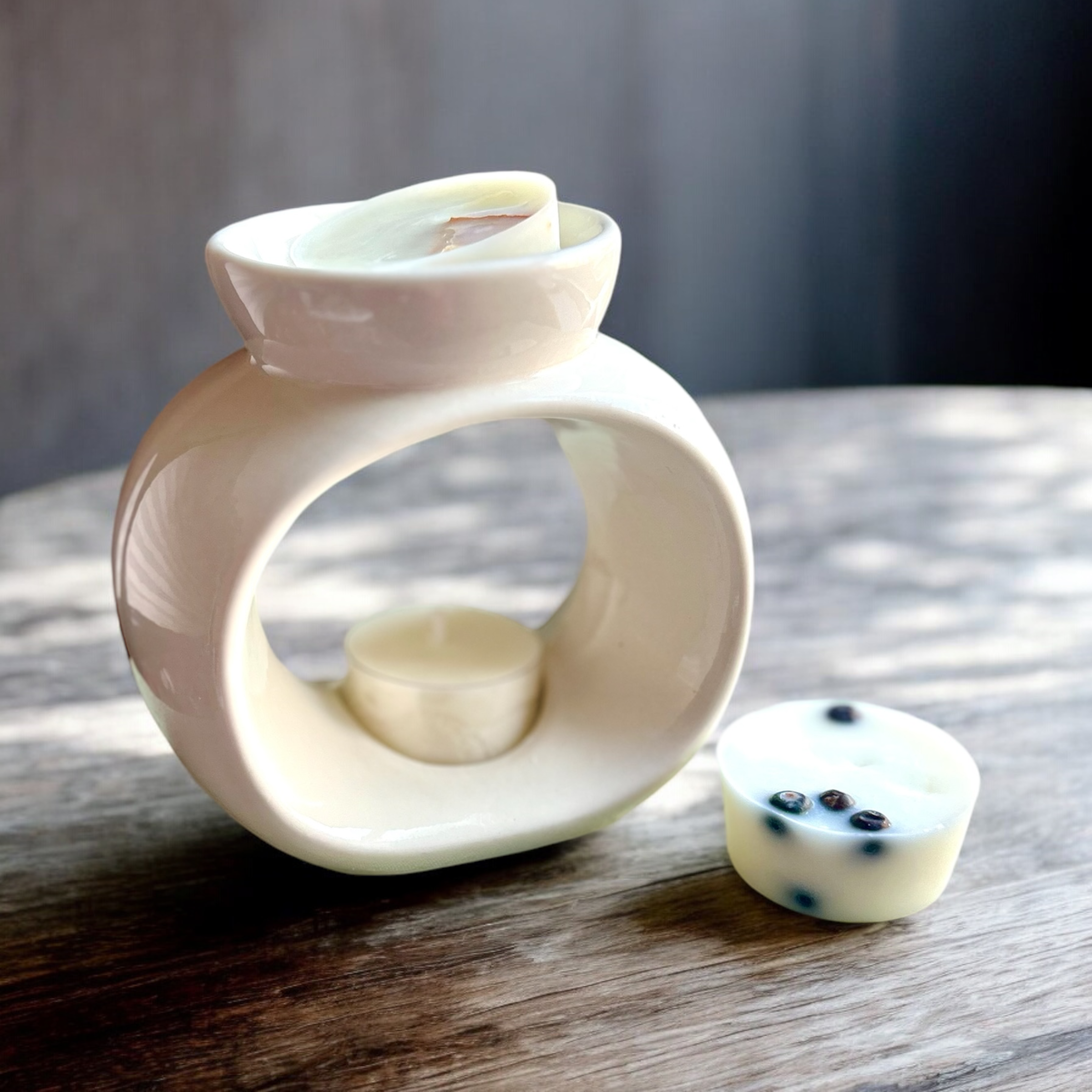 Celestial Wax Burner - Gloss White Ceramic with a rounded opening, an unlit tealight and wax melts on a wooden surface.