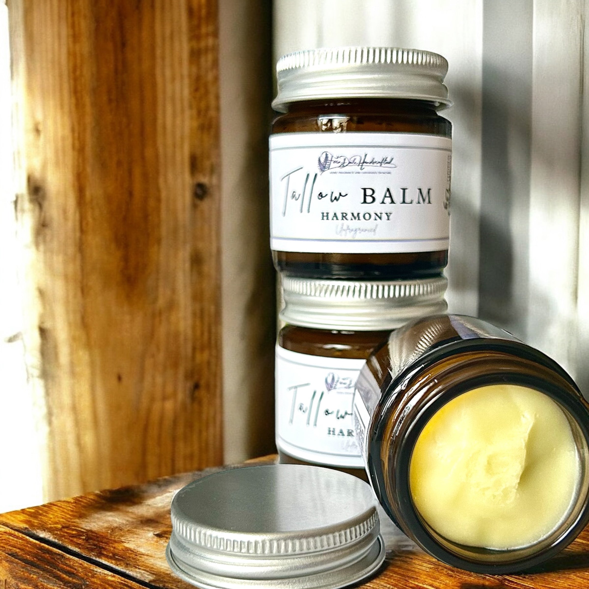 Harmony Tallow Balm in amber jars with silver lids and white labels, one open to reveal pale yellow balm.