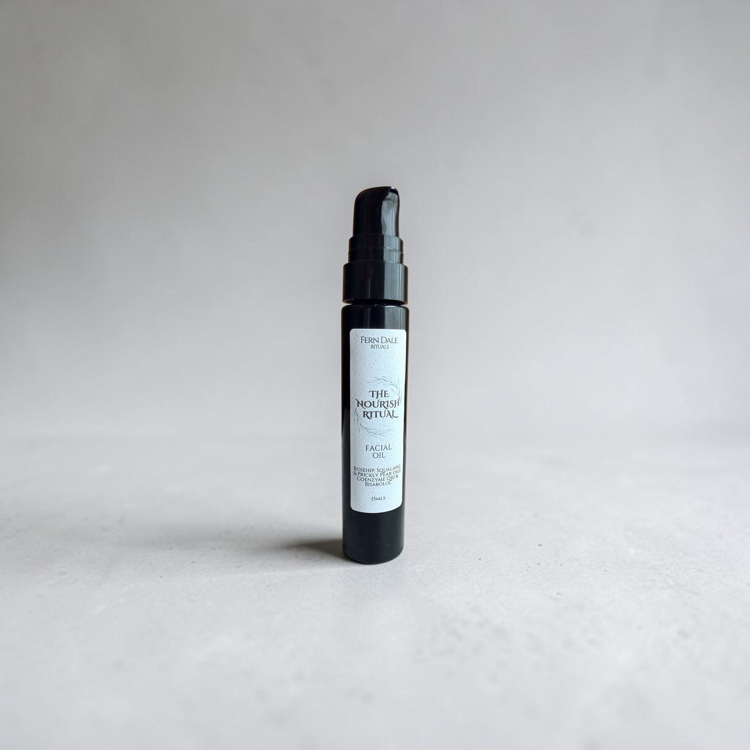The Nourish Ritual - Facial Oil in a slim black pump bottle with a white label on a pale grey surface.