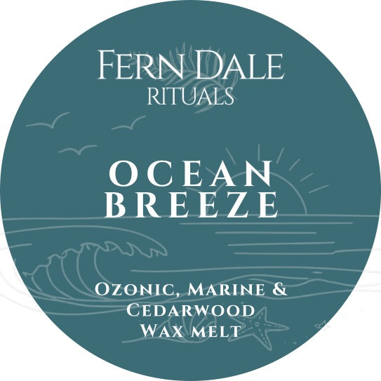 Ocean Breeze round teal label with white lettering and line drawings of waves, seabirds, a sun and starfish.