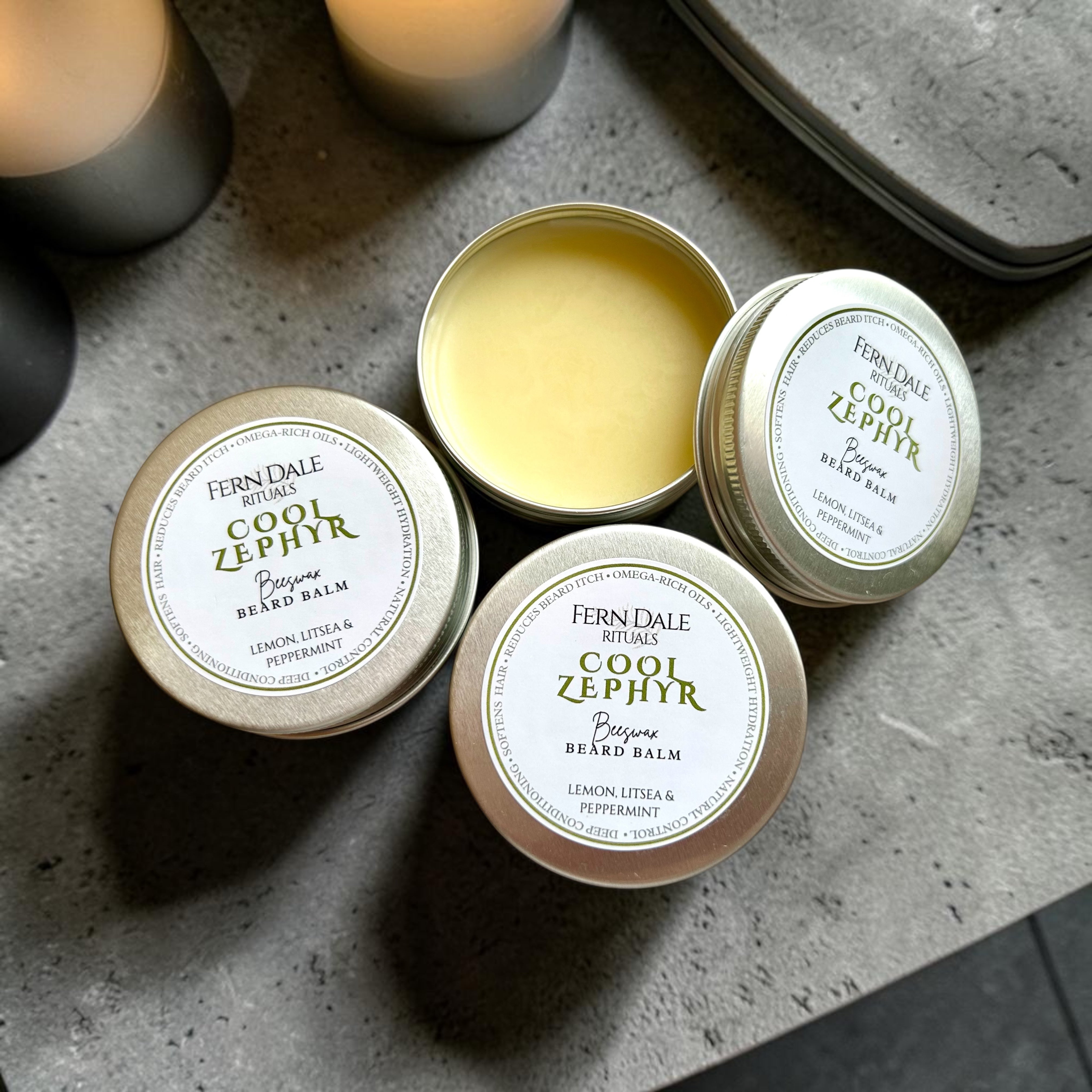 The Beeswax Beard Balm Collection in silver tins on a grey surface, with one open tin showing pale yellow balm.